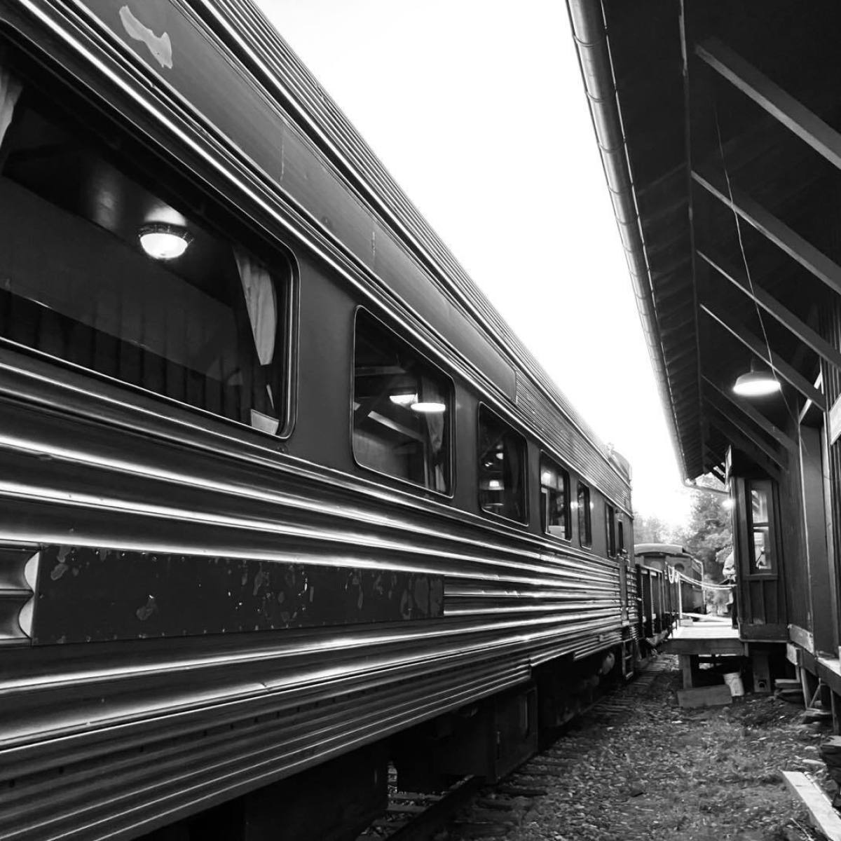 Black and white photo of a train beside a wooden station building.