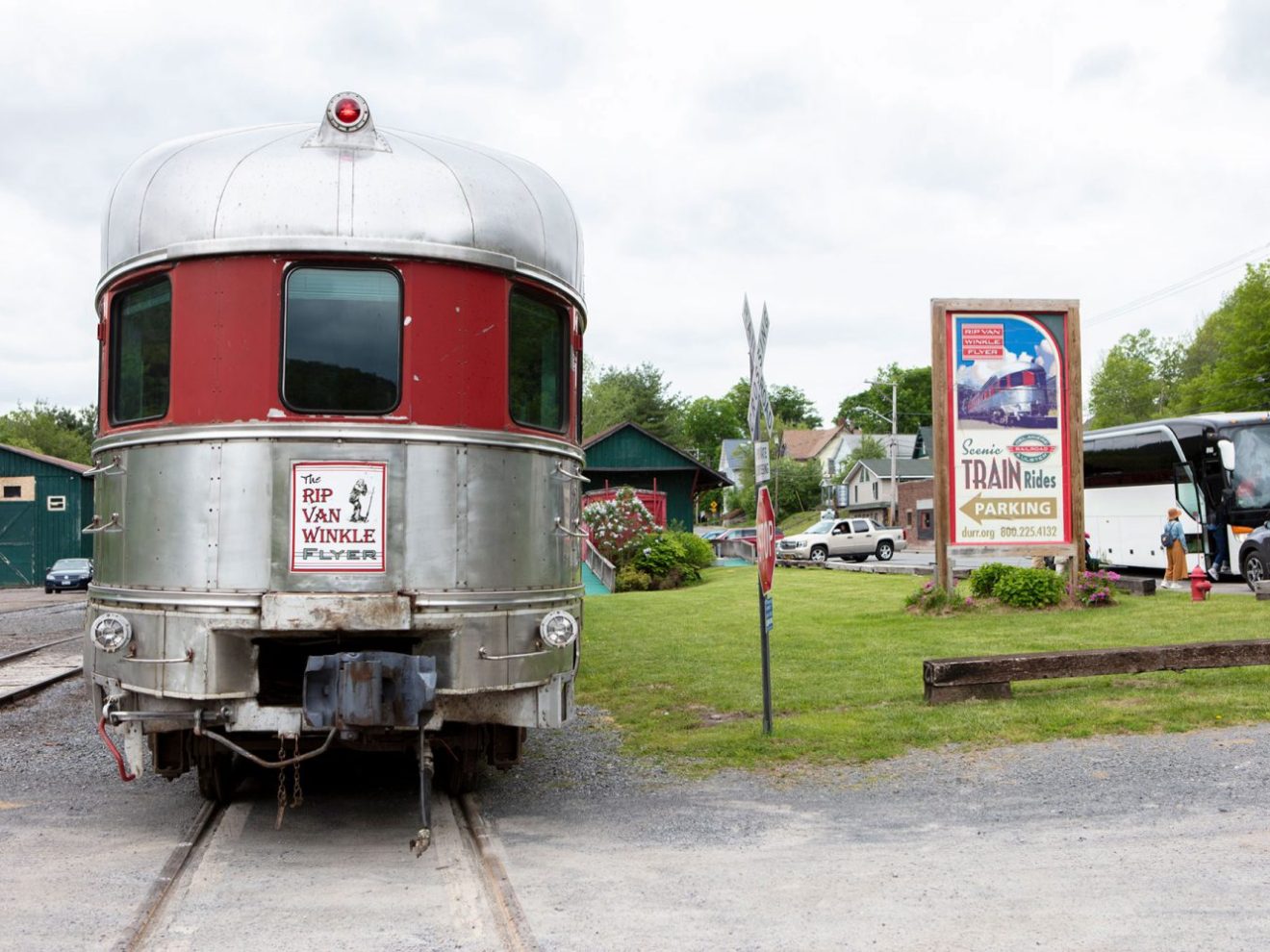 Vintage train car with 'Rip Van Winkle Flyer' sign and nearby bus, buildings, and train ride sign.