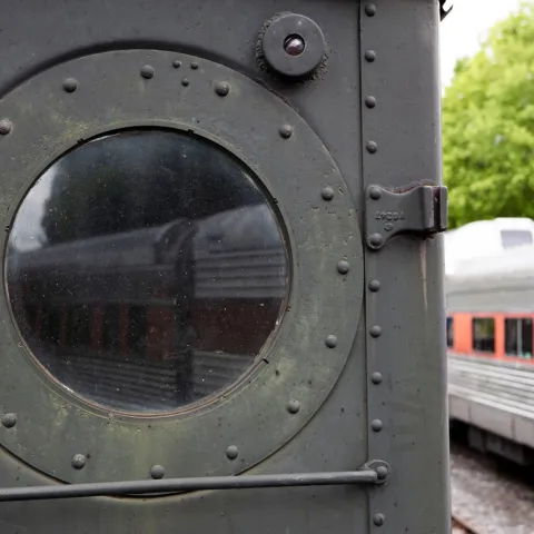 Round window on vintage train door with another train visible outside.