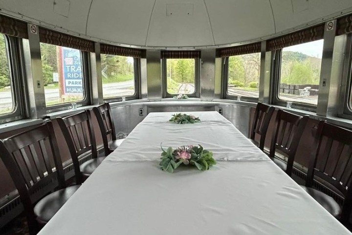 Dining table with flowers in a vintage train car with large windows and surrounding chairs.