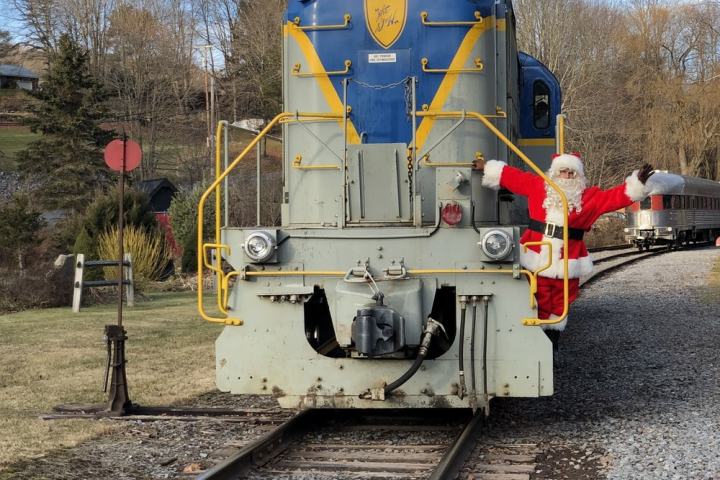Santa Claus waving from side of a blue train on railroad tracks.