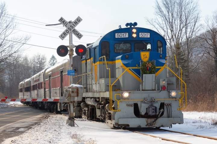 Blue and yellow train crossing snowy road with railroad sign and gate down.