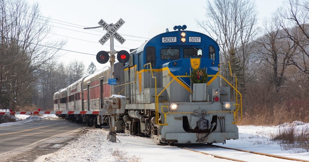 Blue and yellow train crossing snowy road with railroad sign and gate down.