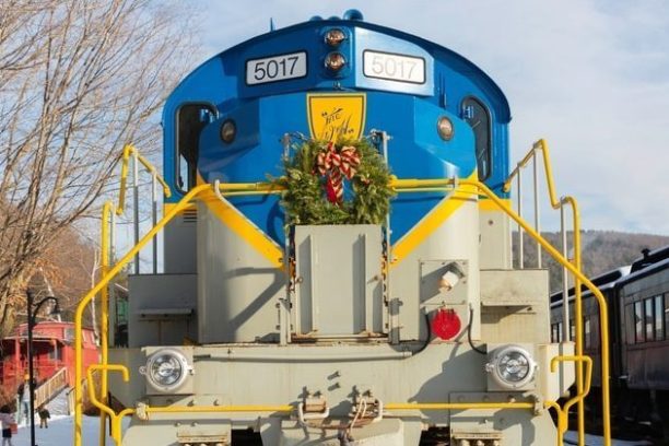 Front view of a blue and yellow train engine with festive wreath on snowy tracks.
